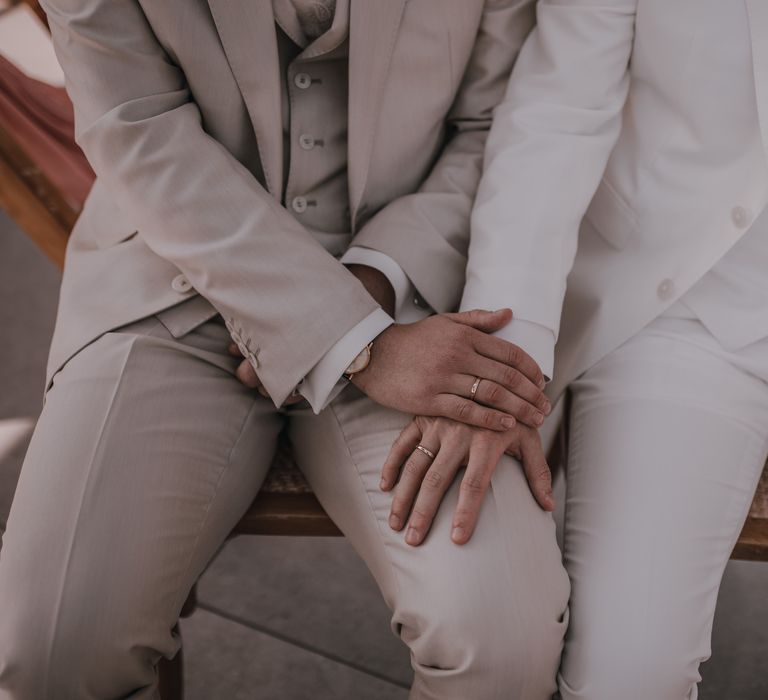 Groom in light grey wedding suit holds hand with husband