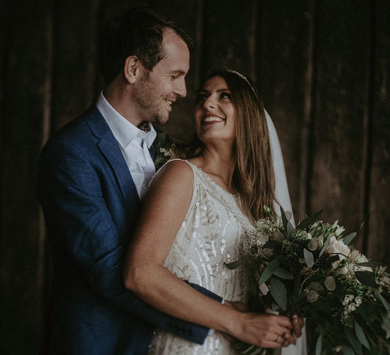 Bride looks back at groom on their wedding day as he embraces her from behind