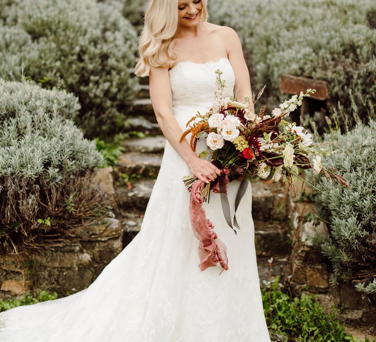 Bride wearing a strapless wedding gown with lace detail, holding a bouquet of wild roses, gerberas and wild grass