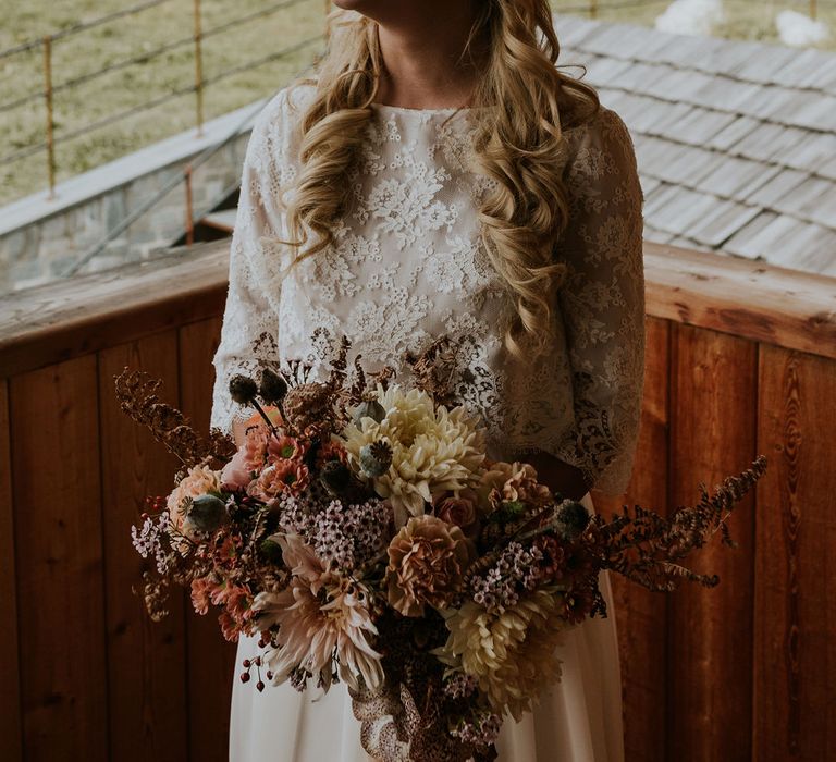 Beautiful bride in a lace wedding dress on her wedding morning holding an autumn wedding bouquet with dahlias