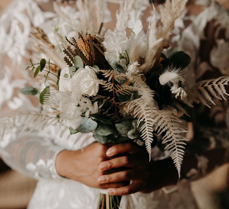 Bride holds white floral bouquet with pampas grass and eucalyptus leaves and green foliage