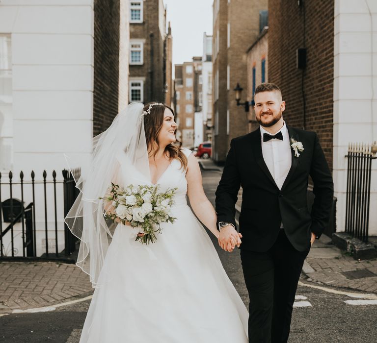 Bride looks lovingly at groom on their wedding day as they walk hand in hand