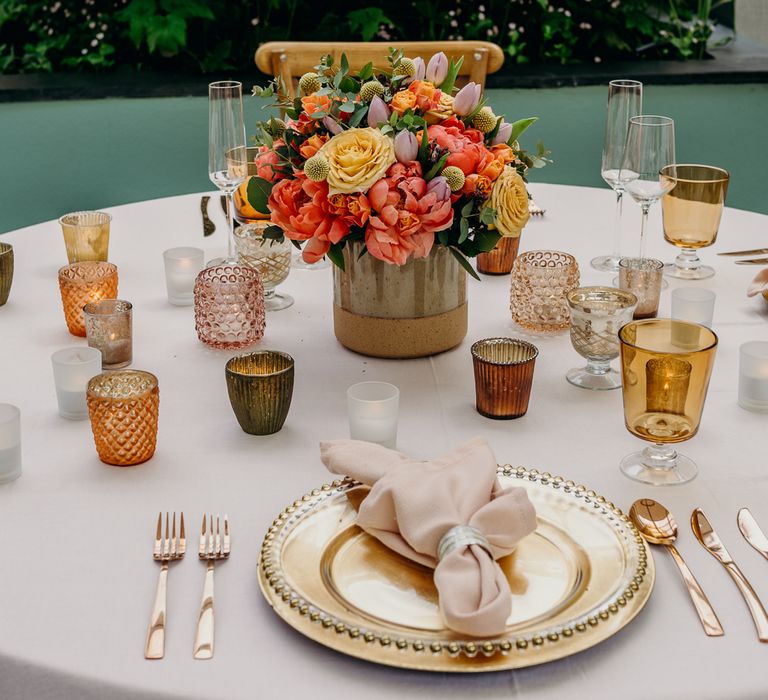 Wedding tablescape for reception with gold plates and pale pink napkins, and bright floral bouquet