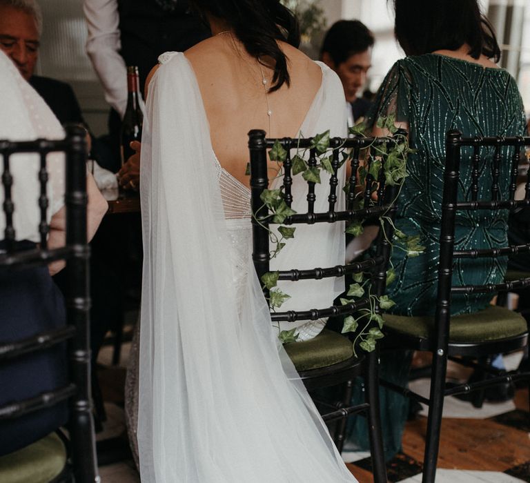 Bride's cape veil of her Eliza Jane Howell wedding dress draping behind her as she is sat down