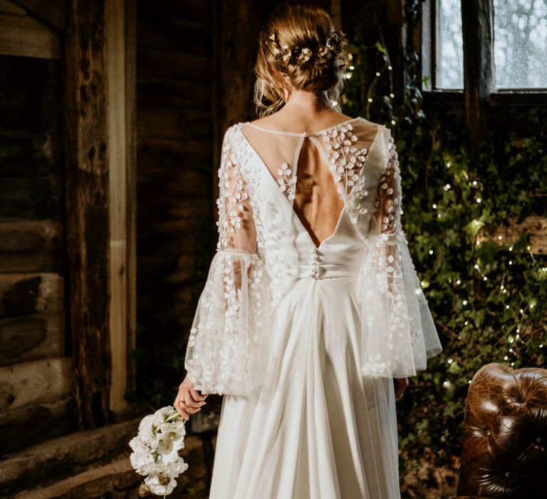 Bride wearing a Delphine Couture wedding dress with open back detail and layered mesh embroidered top with bell sleeves