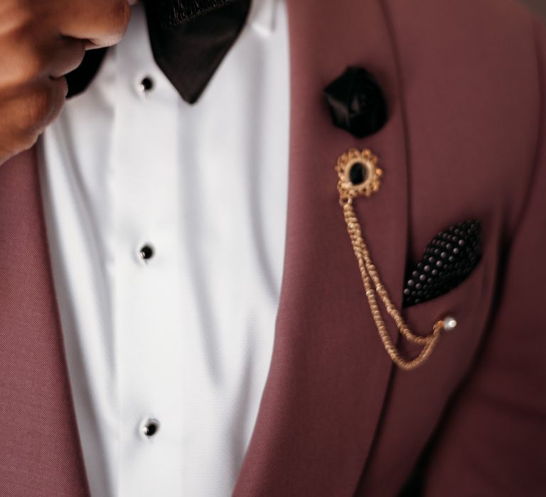 Groom wears black bow tie with deep pink blazer and gold embellishment 