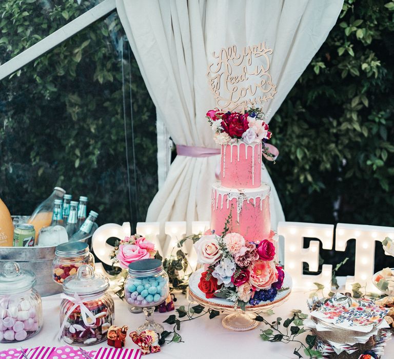 Pink wedding cake with white dripping and floral decor