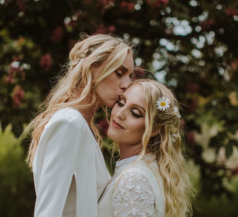 Bride in a wedding cape kissing her bride on the head wearing a long sleeve appliqué wedding dress