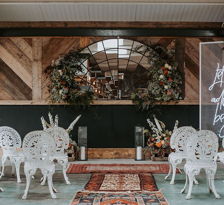 Wedding ceremony at new Lake District wedding Venue, Ghyll Barn with white chairs, mirror backdrop and orange, green and white flowers 