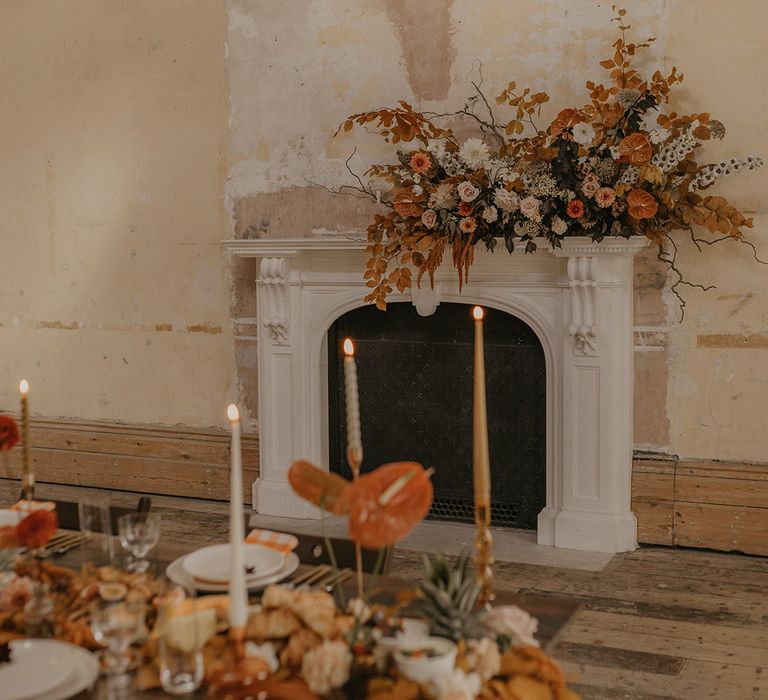 Grand fireplace mantel wedding flowers with brown and orange leaves, anthuriums, and dahlias 