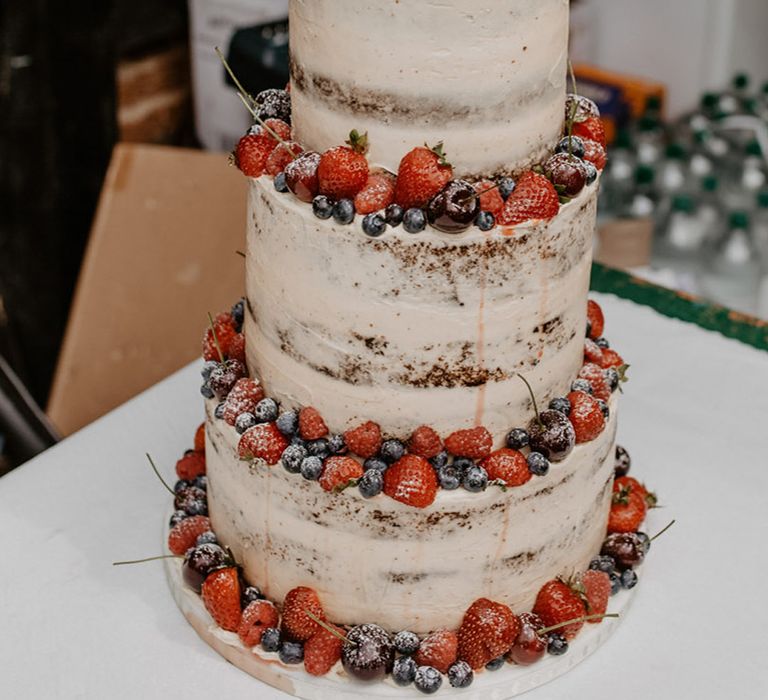 semi naked wedding cake decorated with strawberries, raspberries, blueberries and cherries