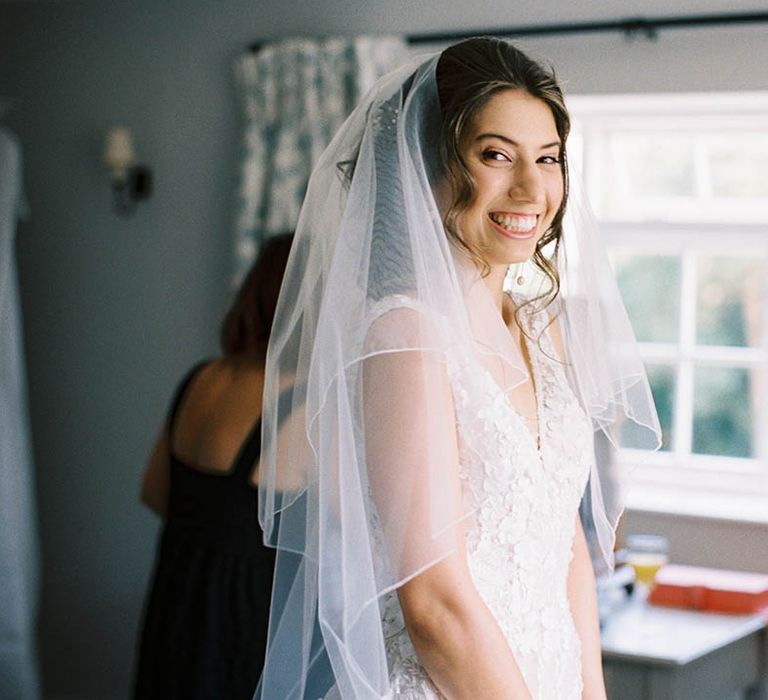 Bride wears long veil and her dark hair in curls on the morning of her wedding day