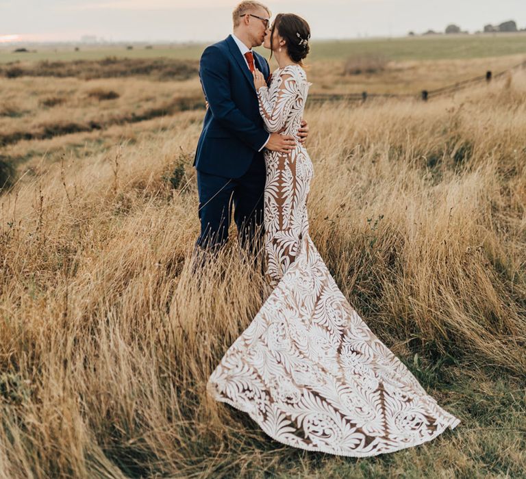 Bride in lace long wedding dress kisses Groom in three piece suit in pampas field 