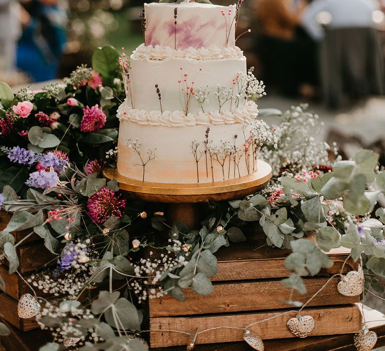 Rustic three-tier wedding cake complete with white frosting and small floral decor with eucalyptus 