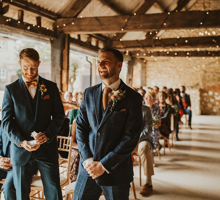 Groom in blue check suit waits for bride at ceremony at East Afton Farmhouse venue