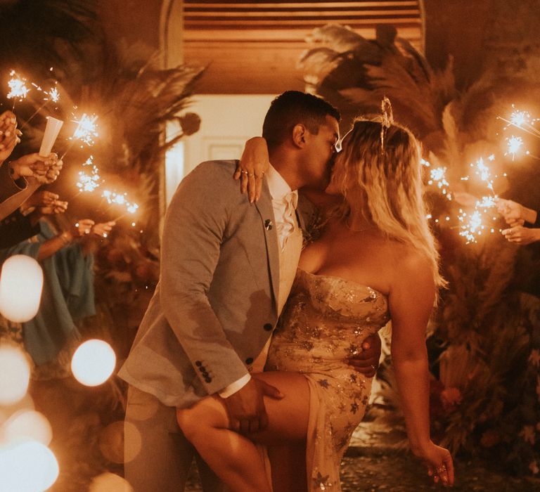 Groom dips back his bride as wedding guests hold sparklers around them