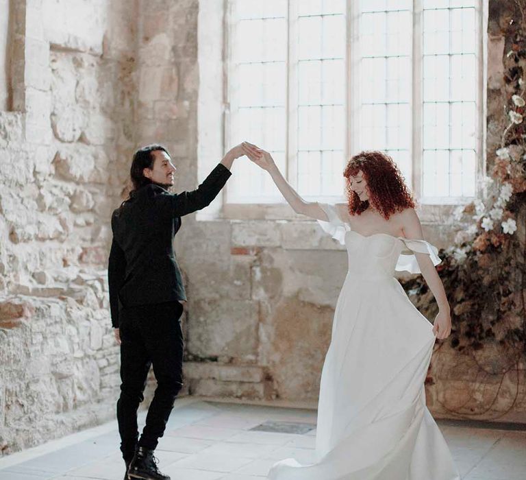 Groom in a black suit with long hair dancing with his bride in a strapless wedding dress with naturally curly hair at the Blackfriars Priory wedding venue 