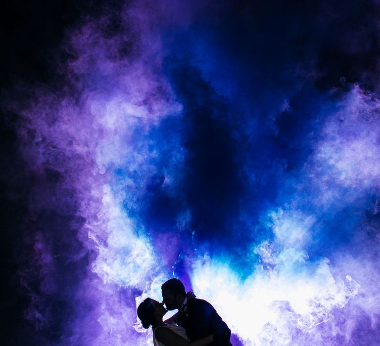 Bride & groom let off blue and purple smoke bomb outdoors on their wedding day