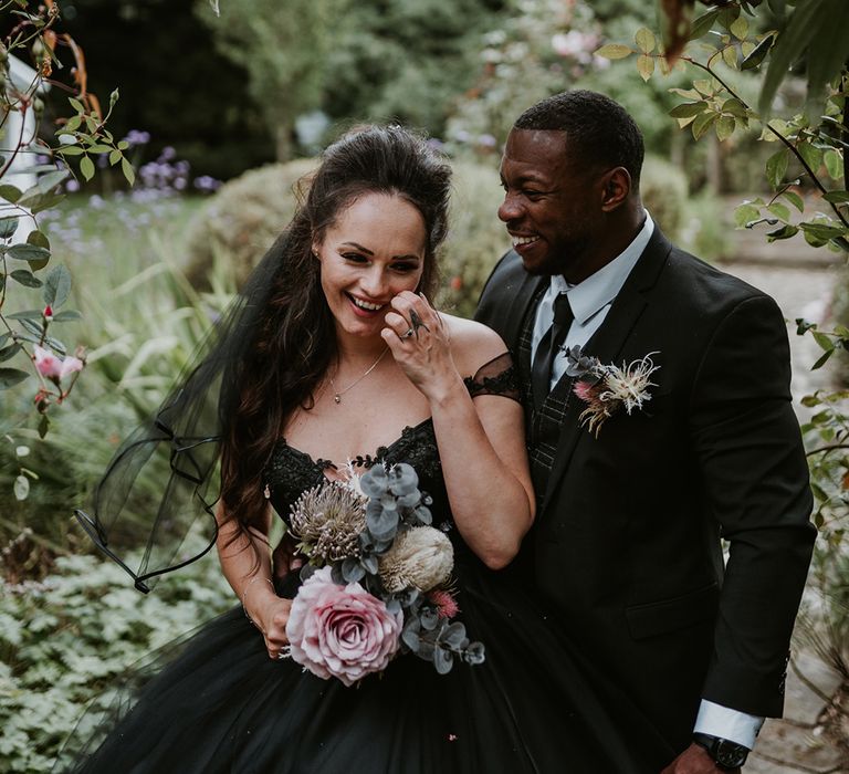 Bride wears black wedding gown whilst holding floral bouquet 