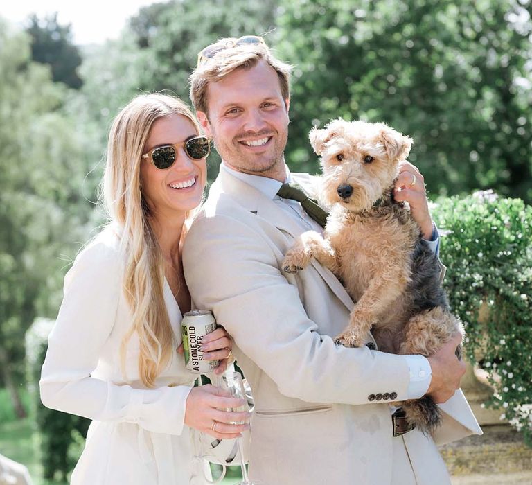 Bride and groom with sunglasses hold their pet dog on their wedding day 