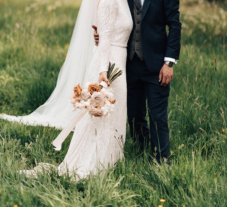 Bride in beaded wedding dress with low back with groom in dark blue suit with gold watch