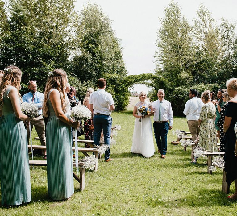 Father of the bride in white shirt and green tie walks bride down the aisle for outdoor ceremony