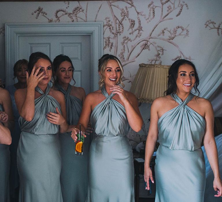 Bridesmaids in mint green halter neck dresses get their first look at the bride