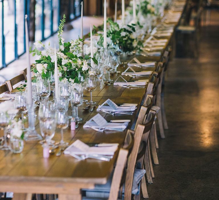 Tall white tapered candles with white flowers and greenery for table settings at classic style wedding