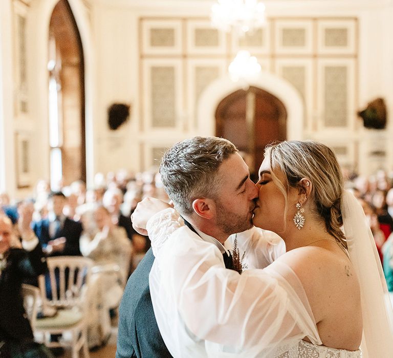 Bride with dangly diamanté earrings has first kiss with groom as a married couple in stunning venue