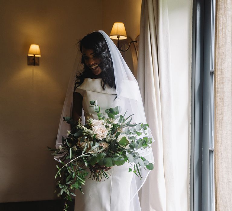 Bride holding wedding bouquet with lots of foliage and white roses in off the shoulder wedding dress and veil 