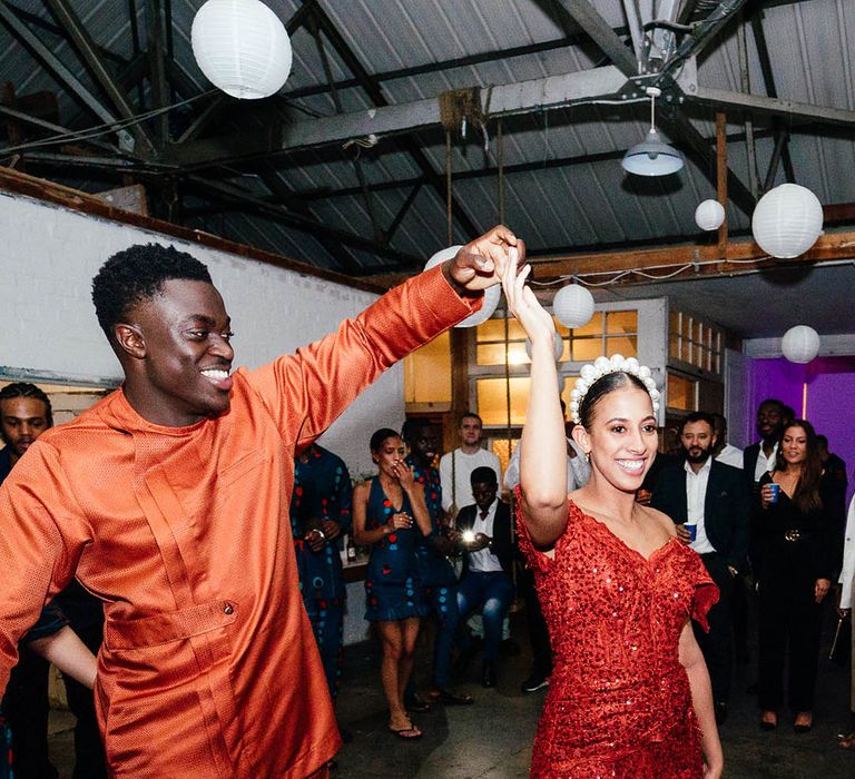 Bride and groom have an outfit change into orange Sierra Leonean outfits for reception with sparkles and pearl headband