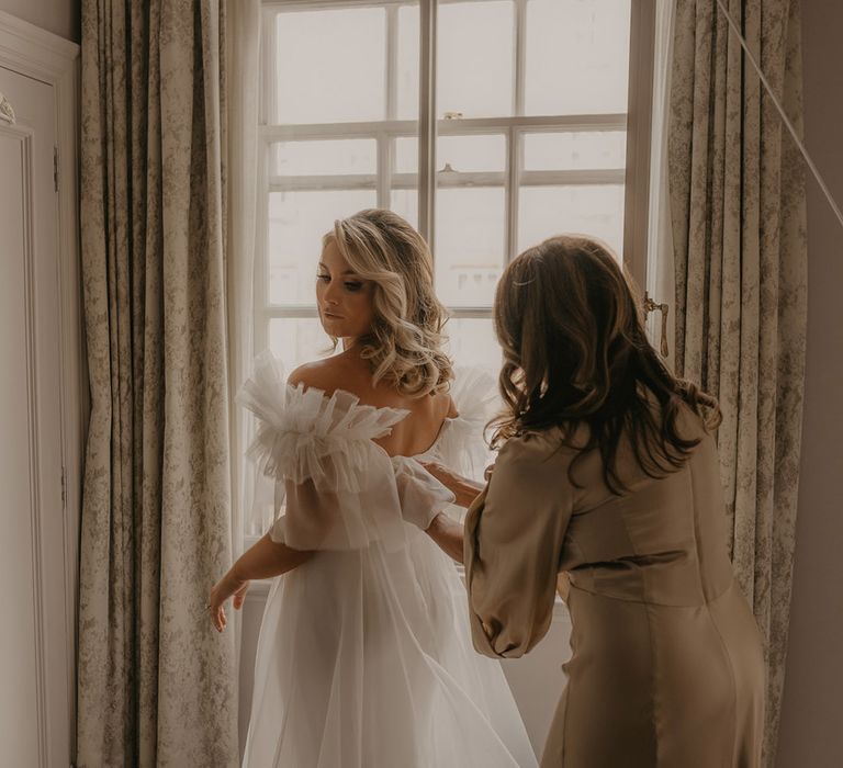 Wedding guest helps the bride into her ruffle wedding dress