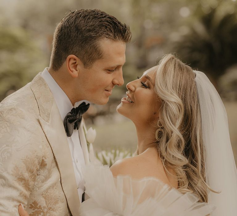 Groom in custom gold patterned tuxedo leans in for a kiss with the bride in ruffle wedding dress