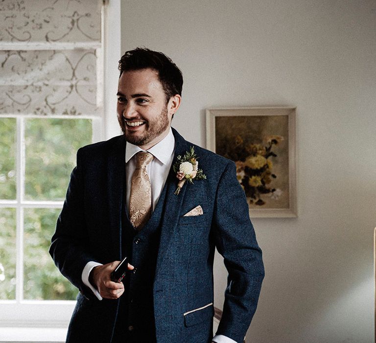 Groom in dark blue suit and gold patterned tie with matching handkerchief and white flower buttonhole