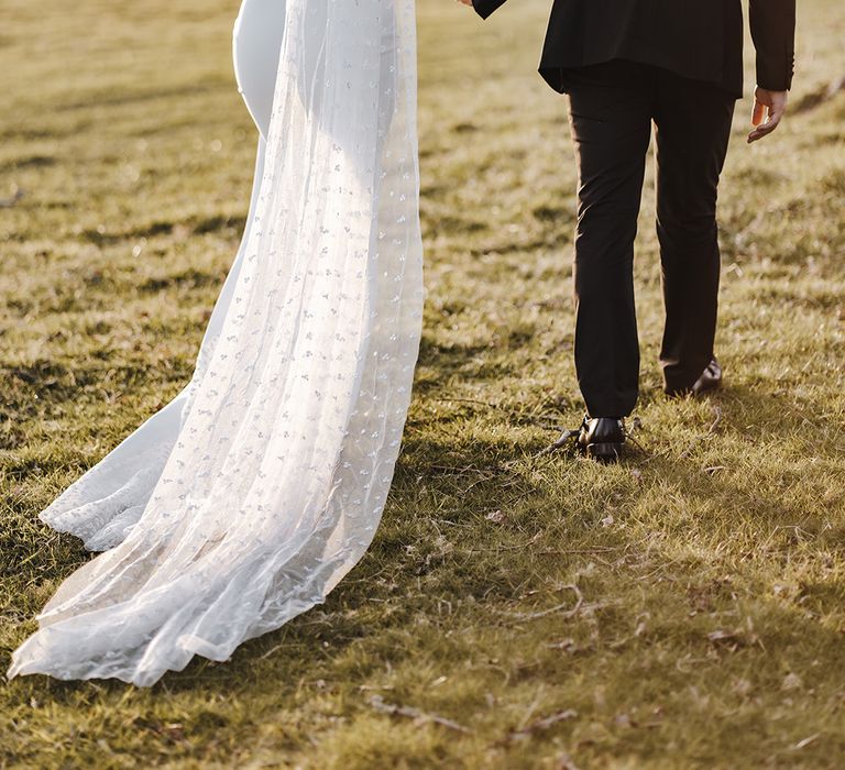 Bride wearing fitted wedding dress with mesh back with dot design wedding dress and matching veil walks with groom