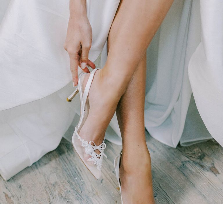 White slingback pointed wedding shoes with sheer lace front with tied white bow ribbon and floral design 