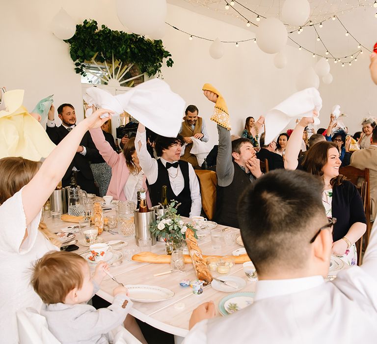 Wedding guests wave their napkins in celebration of the couple with white lantern and fairy light decorations 