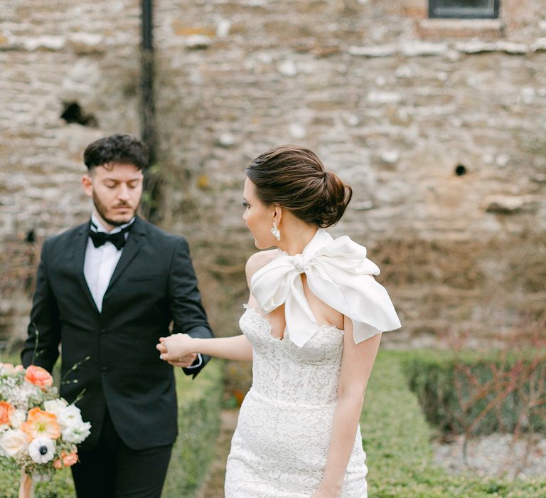 Black tie wedding with groom in a tuxedo and loafers and bride in a strapless lace wedding dress with satin bow neck detail and chic wedding hairstyle 