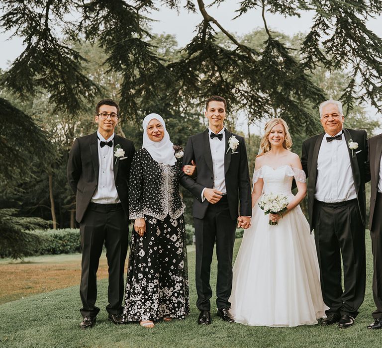 Bride and groom hold hands and pose with the groom's family for classic black tie wedding 