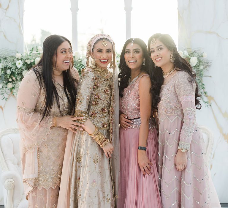 Bride stands with friends who wear pale pink saree's 