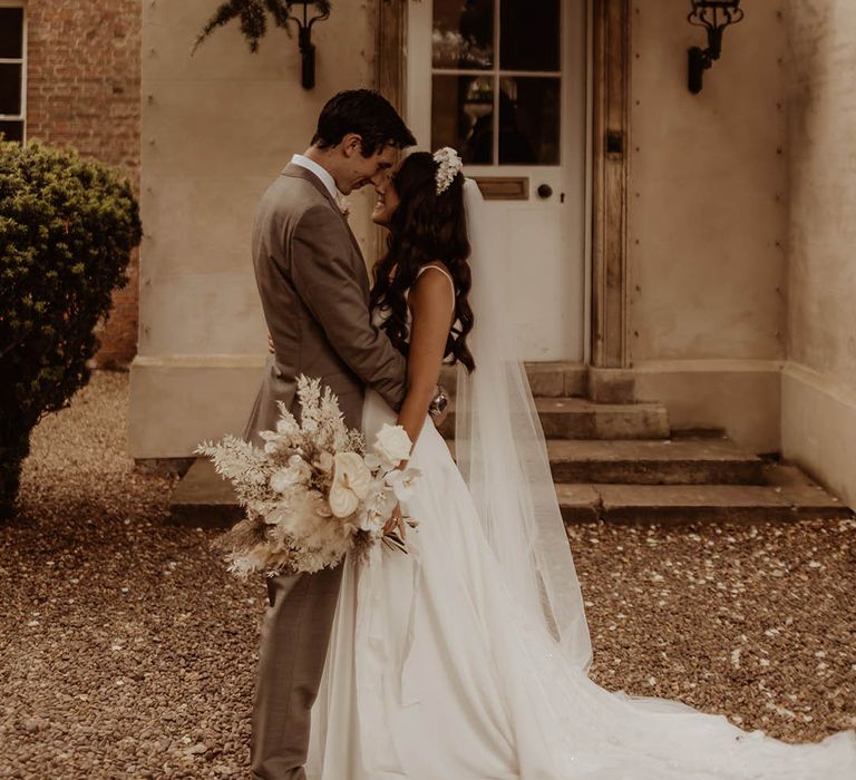 Groom in neutral wedding suit and bride in Alexandra Grecco v-neck wedding dress with bridal headband 