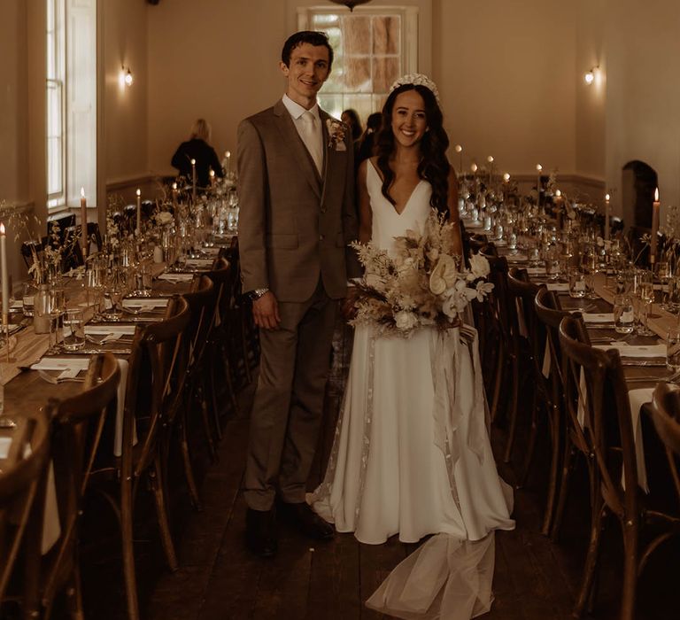 Bride with curled hair in Alexandra Grecco wedding dress with groom in neutral wedding suit smile at the camera