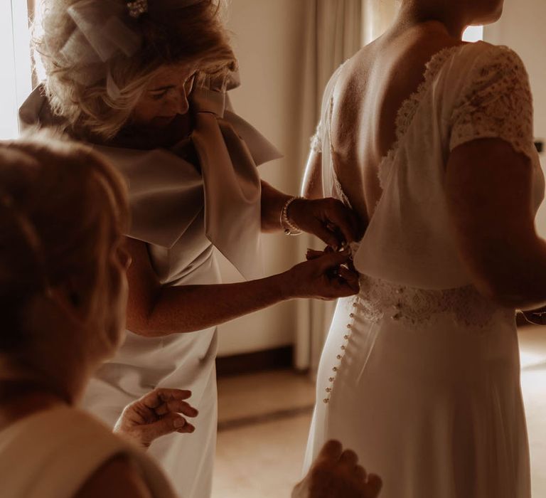 Bride wears low back wedding gown complete with buttons to the back and lace waistband 