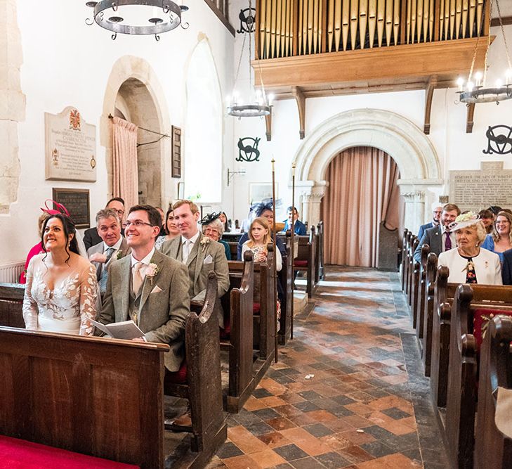 Bride & groom sit at the front of the church during their wedding ceremony surrounded by friends & family