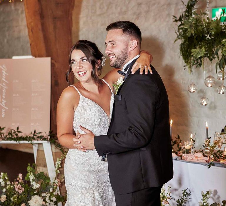 Bride in a fitted lace wedding dress with fishtail design embracing her groom in a tuxedo at their East Riddlesden Hall rustic reception