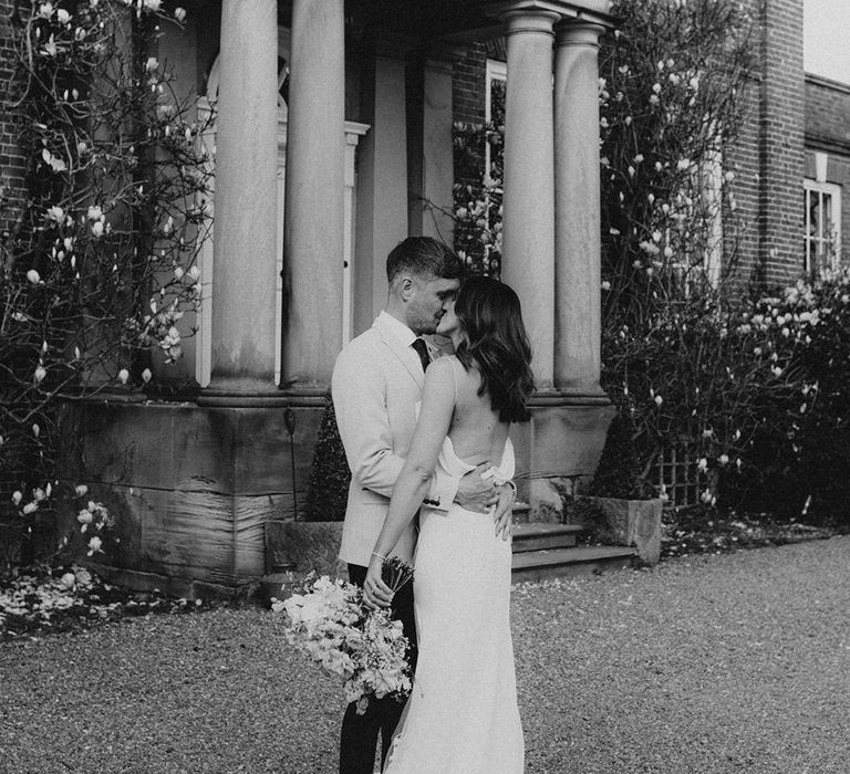 Groom embraces the bride as they share a kiss outside Iscoyd Park wedding venue 