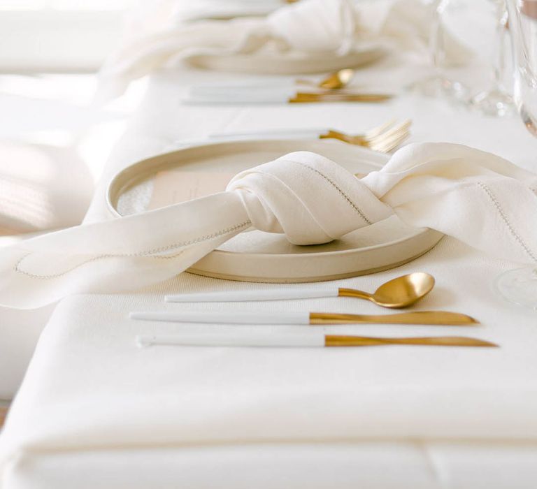 Cream wedding table setting with gold cutlery, ivory napkins and plates for modern and elegant wedding 