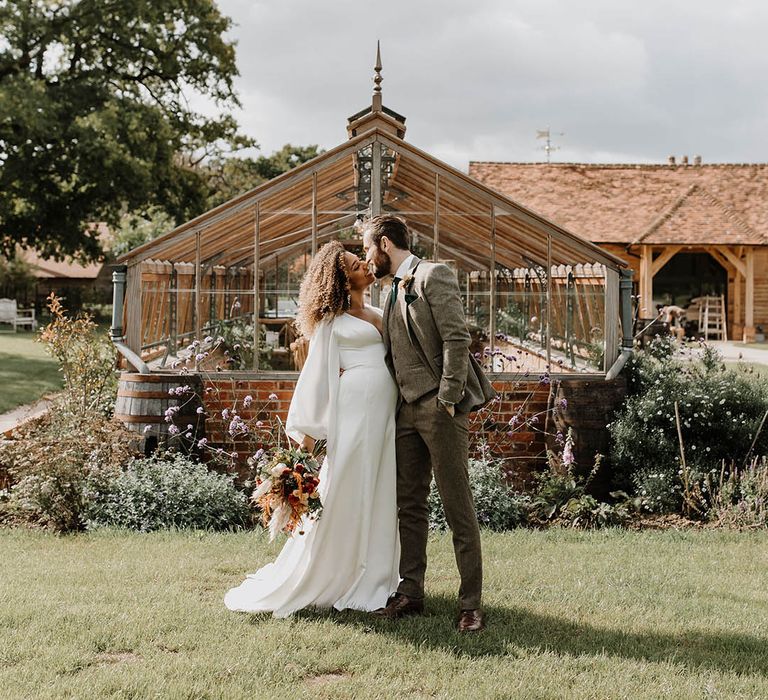 Bride and groom share a kiss in front of their glasshouse reception wedding venue 