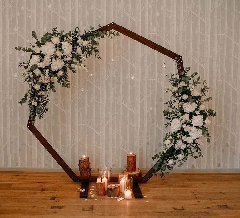 Hexagon wedding arch complete with white florals and green foliage and candles