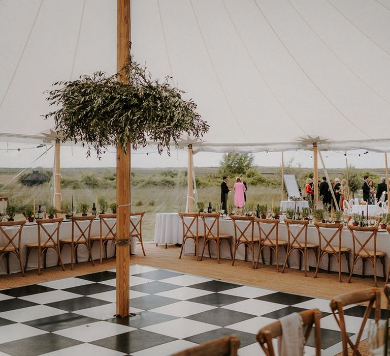 White marquee wedding reception with a black and white checkerboard dance floor with lots of greenery